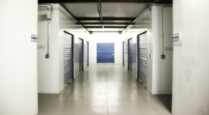 A well lit hallway of large indoor storage units with blue doors