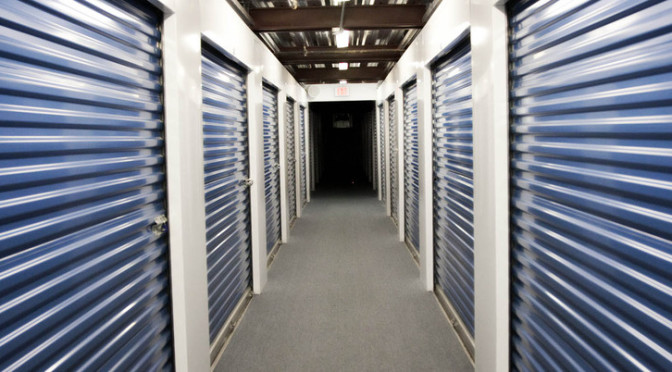 A clean hallway of indoor storage units with blue doors