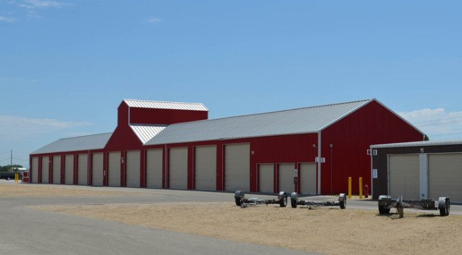 A distance view of an outdoor storage unit facility with differ sized units and an area for parked trailers