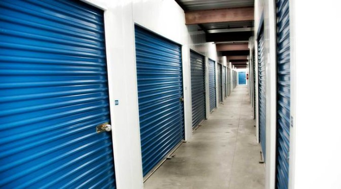A clean well lit hallway of indoor storage units with blue doors and door locks