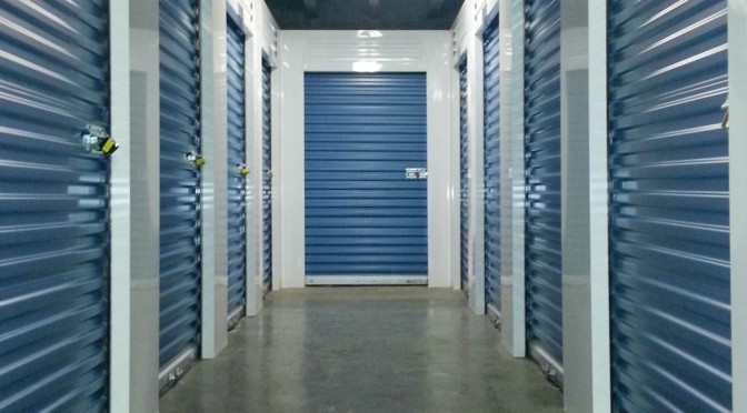 Clean, well lit hallway of indoor storage units with blue doors and locks