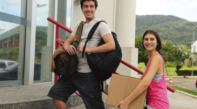 Young couple moving into dorm room smiling at camera