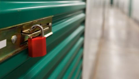 A small red lock on a indoor green storage unit