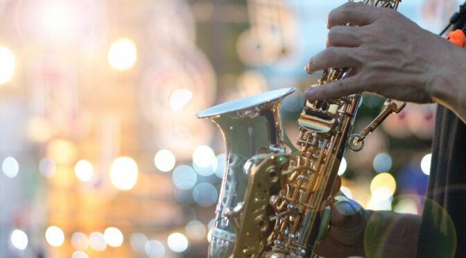 A person holds and plays a saxophone in front of a brightly lit background