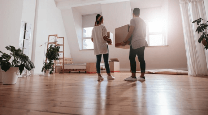 Two people holding moving boxes in an empty room