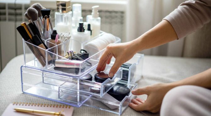 A woman organizes makeup in a clear, acrylic bin with levels and drawers.