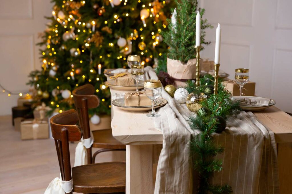 Festive ornaments and decorations on a wooden table next to a Christmas tree.