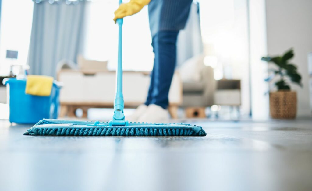 A gloved cleaner using a blue dust mop to clean the floor