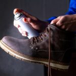 Person is cleaning and spraying agent on men's suede casual boots for protection from moisture and dirt.