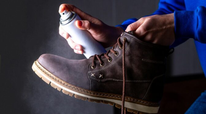 Person is cleaning and spraying agent on men's suede casual boots for protection from moisture and dirt.