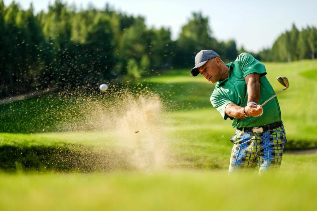 A golfer hits a ball from a bunker with a golf club