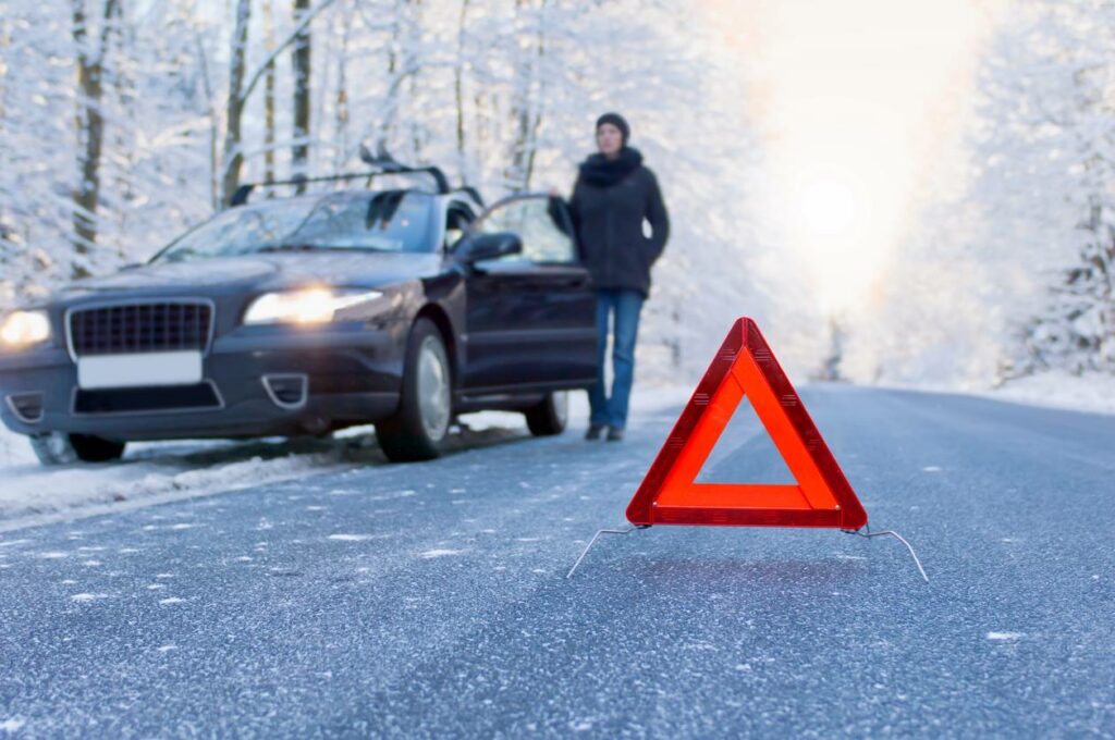 A woman stands by her car with a retroreflector on the road to warn others.