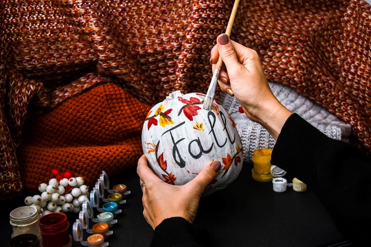 A woman painting “fall” on a pumpkin for Halloween.